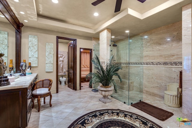 bathroom with vanity, walk in shower, a tray ceiling, ceiling fan, and toilet