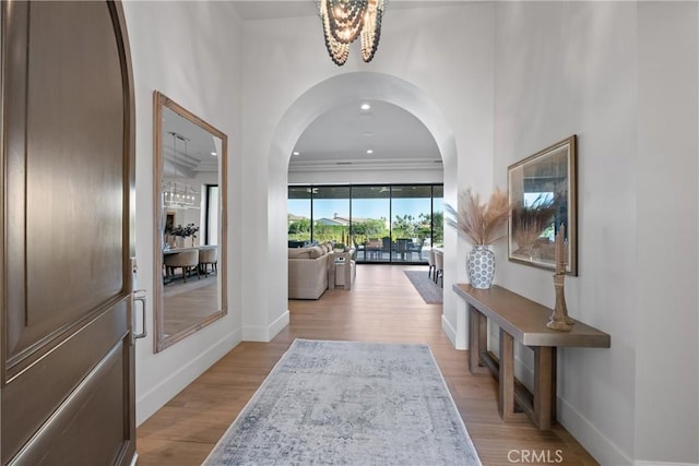 hallway with ornamental molding, floor to ceiling windows, a notable chandelier, and light wood-type flooring