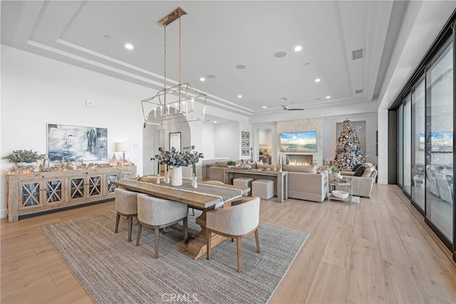 dining area featuring a raised ceiling, ceiling fan, a fireplace, and light wood-type flooring