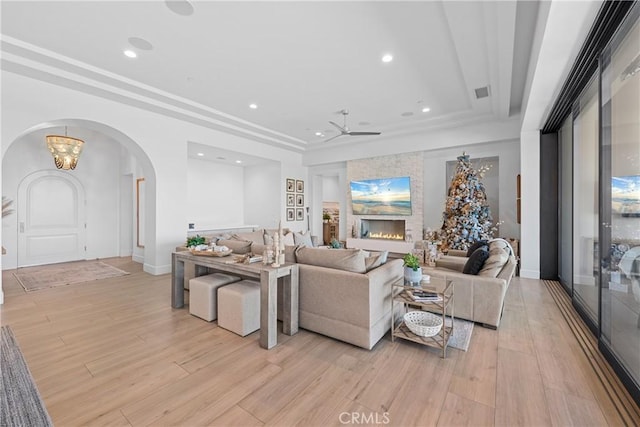 living room with a raised ceiling, ceiling fan, and light hardwood / wood-style flooring