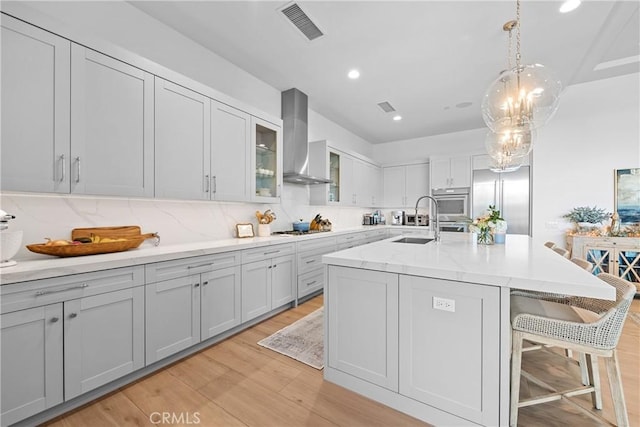 kitchen featuring wall chimney exhaust hood, a breakfast bar, sink, light hardwood / wood-style flooring, and a kitchen island with sink