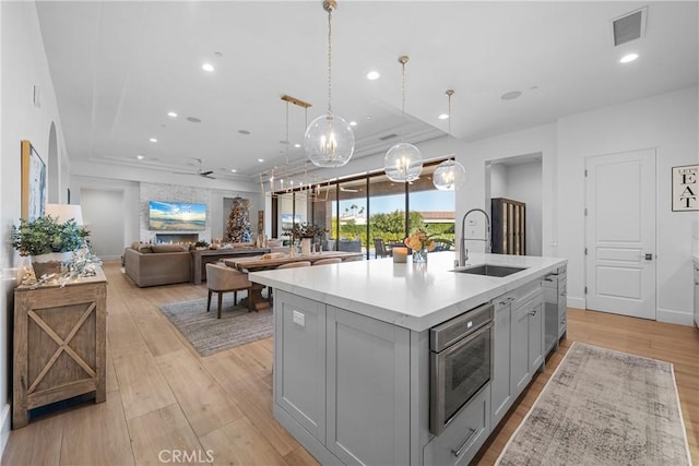 kitchen with sink, light hardwood / wood-style flooring, gray cabinets, hanging light fixtures, and an island with sink