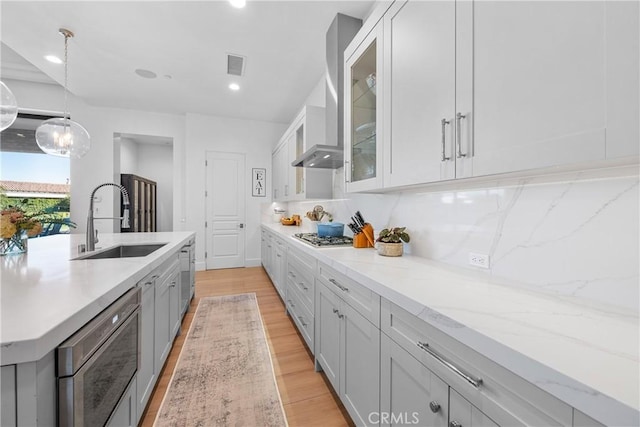 kitchen with pendant lighting, sink, dishwasher, light hardwood / wood-style floors, and light stone countertops