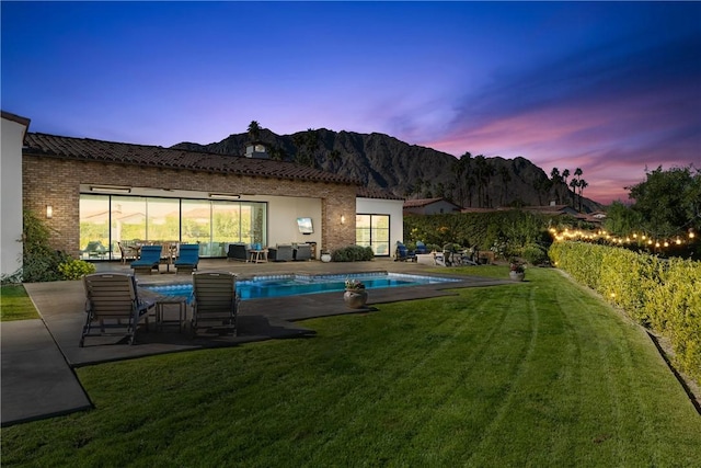 back house at dusk featuring a mountain view, a yard, a patio, and a fenced in pool