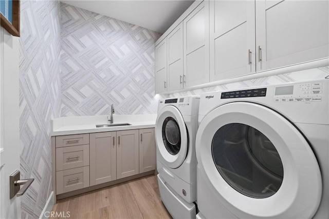 washroom featuring cabinets, sink, washing machine and clothes dryer, and light wood-type flooring