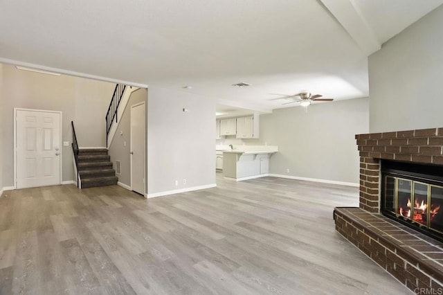 unfurnished living room featuring a brick fireplace, light hardwood / wood-style flooring, and ceiling fan