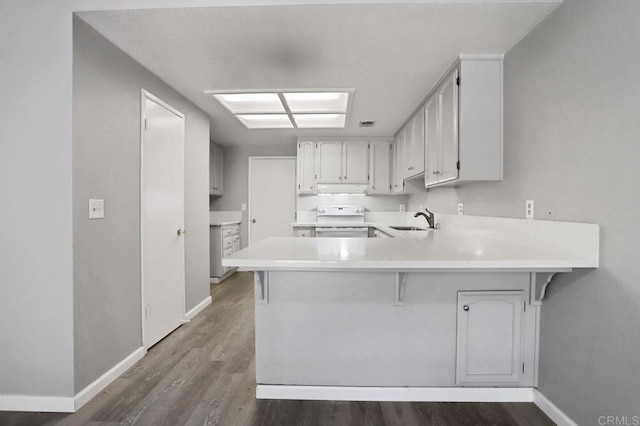 kitchen featuring white range, kitchen peninsula, sink, dark hardwood / wood-style floors, and white cabinetry