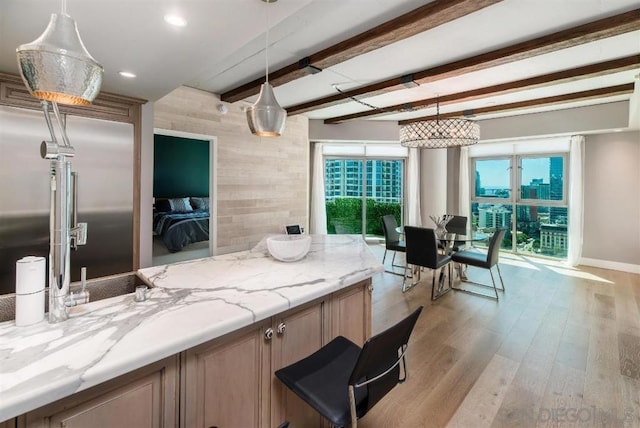 kitchen with light stone counters, hanging light fixtures, light hardwood / wood-style flooring, and beam ceiling