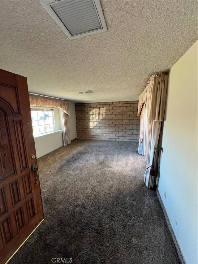 empty room with carpet floors, a textured ceiling, and brick wall