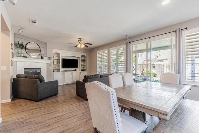 dining space featuring a fireplace, ceiling fan, built in features, and hardwood / wood-style flooring