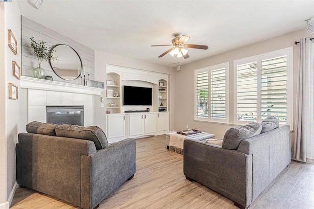 living room with a tile fireplace, ceiling fan, built in features, and light hardwood / wood-style floors