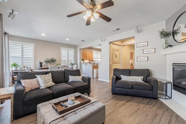 living room featuring a fireplace, light hardwood / wood-style flooring, and ceiling fan