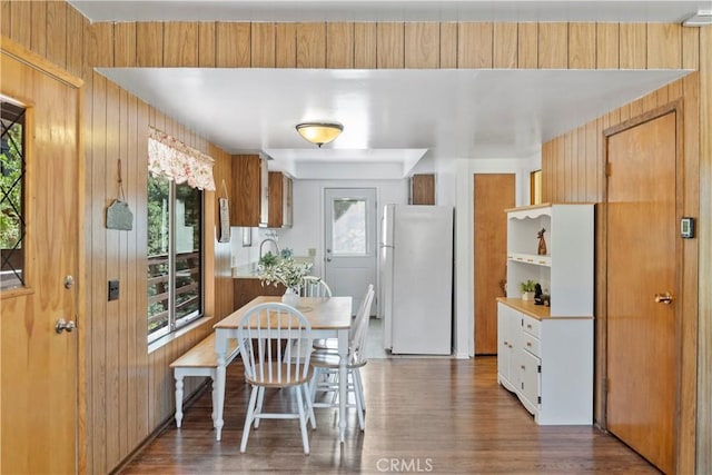 kitchen with white fridge, dark wood-type flooring, and wooden walls