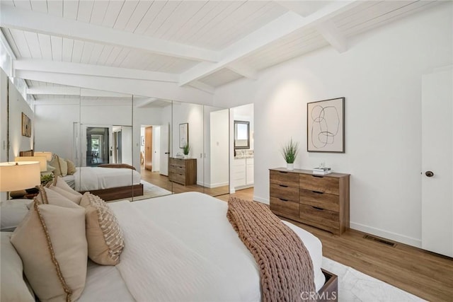 bedroom featuring ensuite bathroom, lofted ceiling with beams, and light wood-type flooring