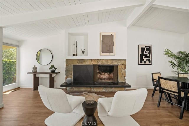 living room with lofted ceiling with beams, hardwood / wood-style flooring, and a stone fireplace