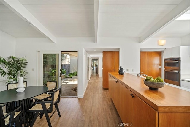 kitchen with double oven, kitchen peninsula, beamed ceiling, and light wood-type flooring