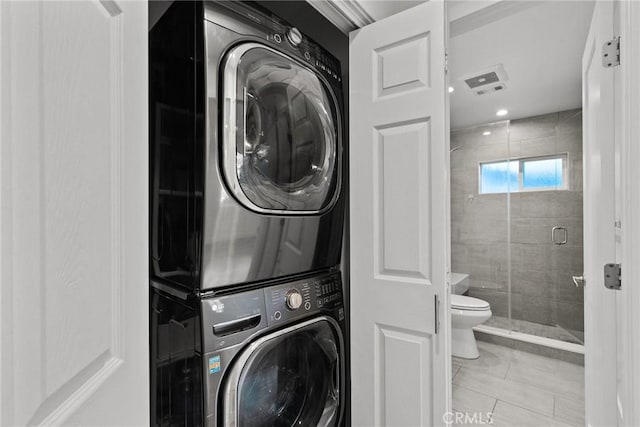 clothes washing area featuring light tile patterned floors and stacked washing maching and dryer