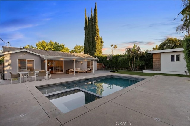 pool at dusk featuring an in ground hot tub, a patio, and an outdoor hangout area