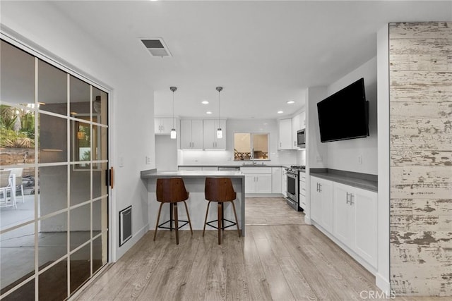 kitchen featuring appliances with stainless steel finishes, a breakfast bar, light hardwood / wood-style flooring, white cabinetry, and hanging light fixtures