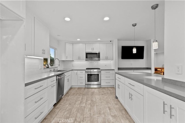 kitchen featuring white cabinetry, sink, light hardwood / wood-style flooring, pendant lighting, and appliances with stainless steel finishes