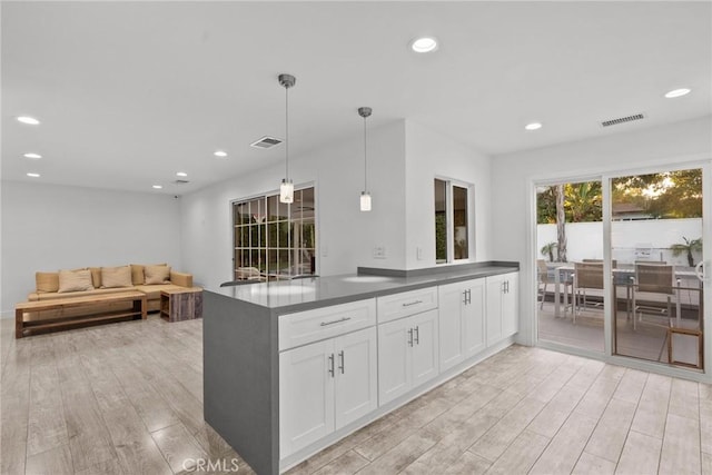 kitchen featuring kitchen peninsula, white cabinetry, light hardwood / wood-style flooring, and pendant lighting