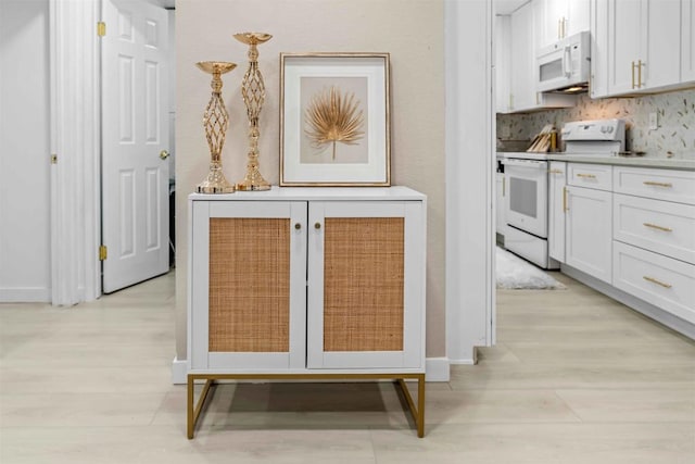 kitchen with light wood-type flooring, white appliances, white cabinetry, and tasteful backsplash