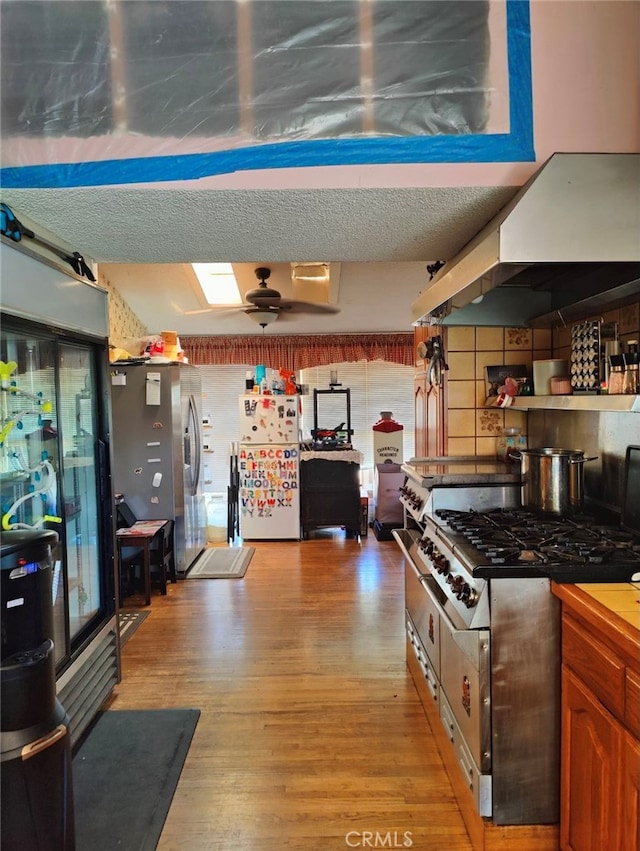 kitchen with light wood-type flooring, a textured ceiling, stainless steel range, and white fridge