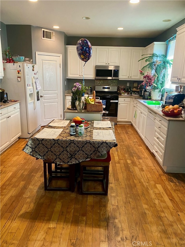 kitchen with appliances with stainless steel finishes, white cabinetry, a center island, and light hardwood / wood-style flooring