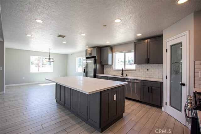 kitchen with pendant lighting, sink, appliances with stainless steel finishes, a center island, and light wood-type flooring