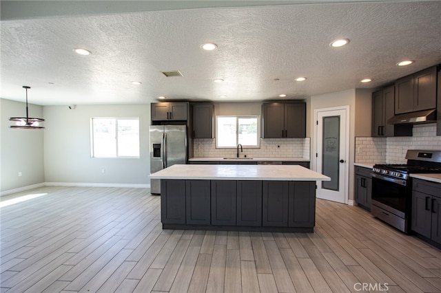 kitchen with appliances with stainless steel finishes, a kitchen island, sink, and range hood