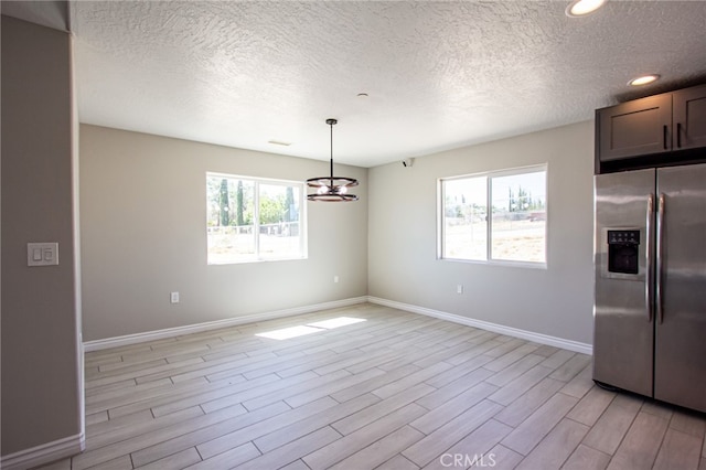 unfurnished dining area featuring a notable chandelier, light hardwood / wood-style flooring, plenty of natural light, and a textured ceiling