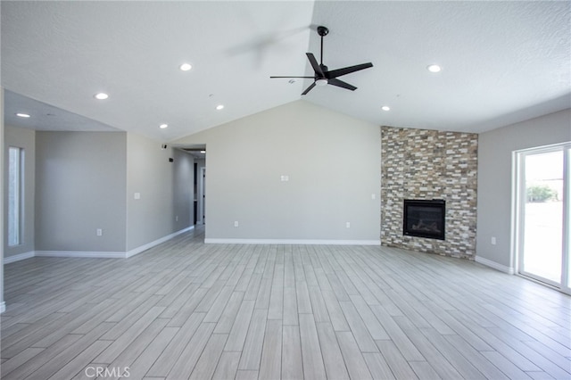 unfurnished living room featuring light hardwood / wood-style flooring, a large fireplace, lofted ceiling, and ceiling fan