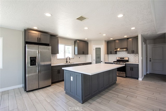 kitchen featuring appliances with stainless steel finishes, light hardwood / wood-style floors, a textured ceiling, a center island, and sink