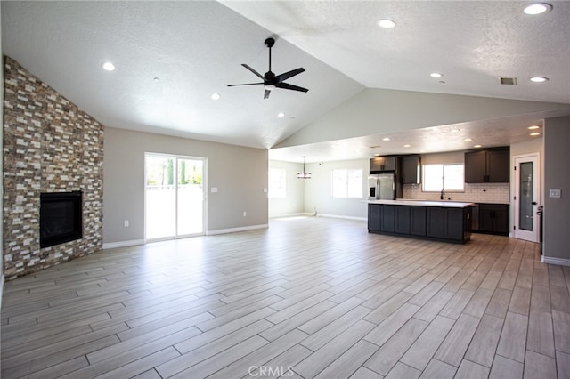 unfurnished living room with high vaulted ceiling, a large fireplace, light hardwood / wood-style floors, and ceiling fan