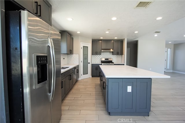 kitchen featuring appliances with stainless steel finishes, backsplash, a textured ceiling, a center island, and light hardwood / wood-style flooring