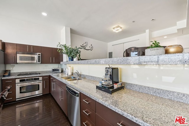 kitchen featuring dark brown cabinetry, sink, dark wood-type flooring, stainless steel appliances, and light stone countertops