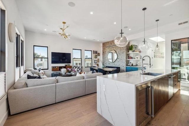 kitchen featuring sink, beverage cooler, hanging light fixtures, a center island with sink, and light wood-type flooring