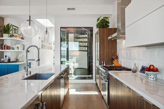 kitchen featuring light stone countertops, appliances with stainless steel finishes, sink, and wall chimney exhaust hood