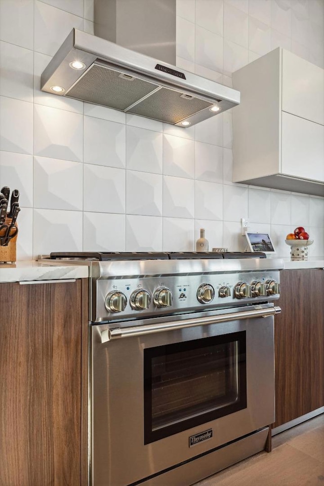 kitchen featuring high end stainless steel range oven, dark brown cabinets, tasteful backsplash, white cabinets, and wall chimney exhaust hood