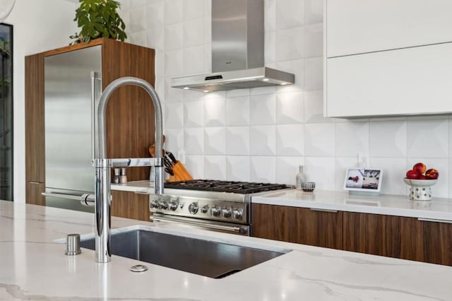 kitchen featuring wall chimney range hood, backsplash, light stone countertops, and white cabinets