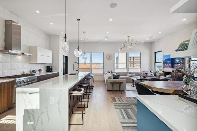 kitchen with light stone countertops, a large island, light wood-type flooring, and wall chimney exhaust hood