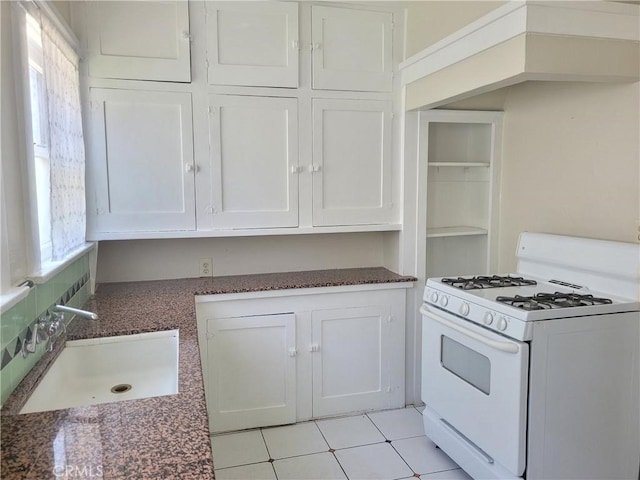 kitchen featuring tasteful backsplash, white gas range, sink, light tile patterned floors, and white cabinetry