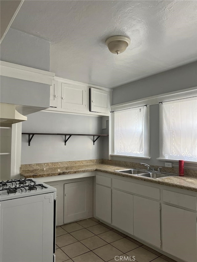 kitchen featuring white cabinetry, sink, light tile patterned floors, and white gas range oven