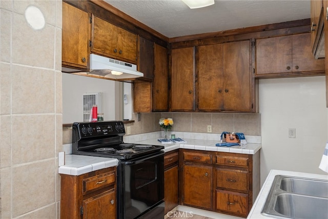 kitchen with exhaust hood, black range with electric cooktop, tile counters, and decorative backsplash