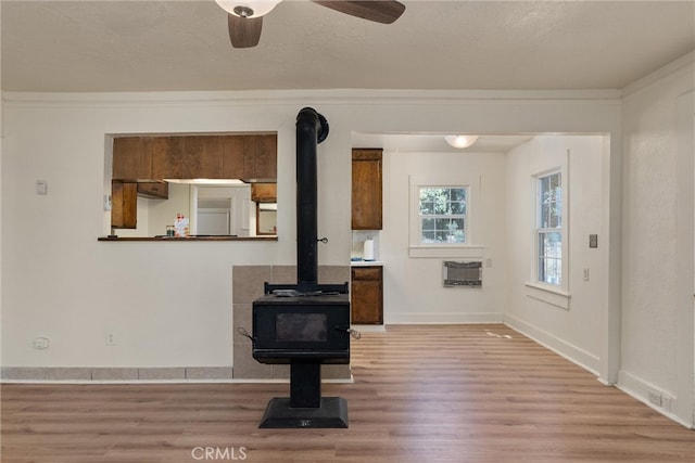 interior space with a wood stove, ceiling fan, hardwood / wood-style flooring, and crown molding