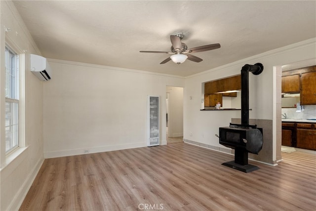 unfurnished living room with light wood-type flooring, a wall unit AC, a wood stove, ornamental molding, and ceiling fan