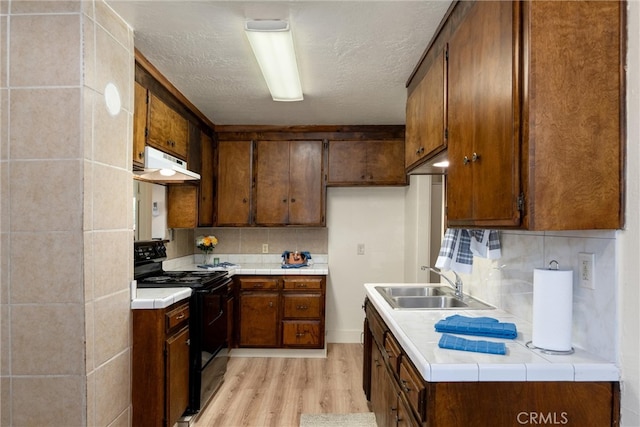 kitchen with decorative backsplash, light hardwood / wood-style flooring, tile counters, sink, and electric range