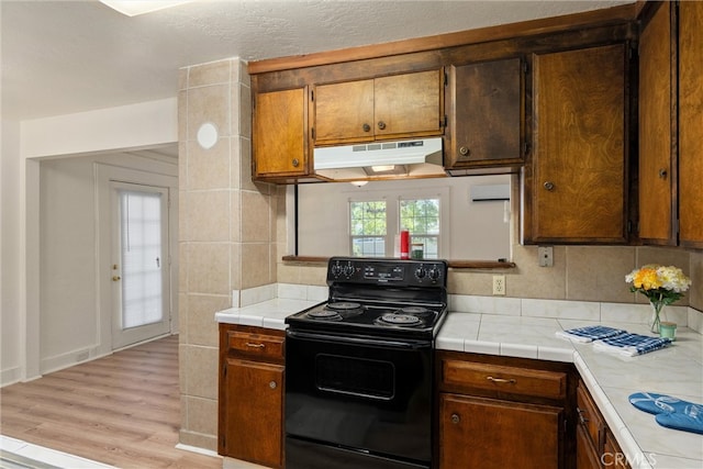 kitchen featuring black / electric stove, light wood-type flooring, tile countertops, and decorative backsplash