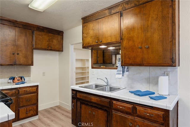 kitchen featuring decorative backsplash, light wood-type flooring, tile countertops, and sink