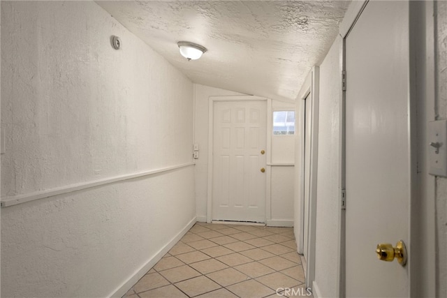 corridor with light tile patterned flooring, lofted ceiling, and a textured ceiling